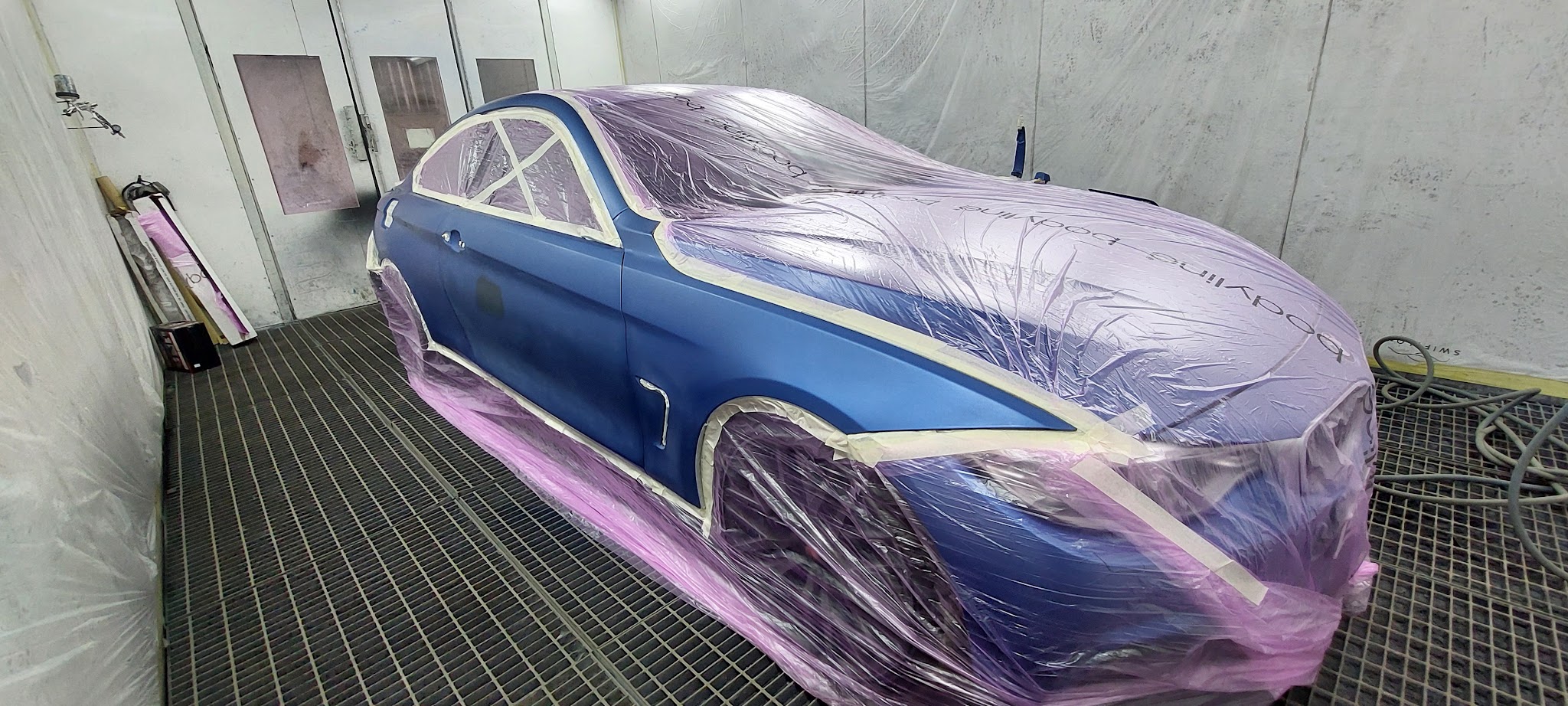 Blue car masked in pink film in the paint booth